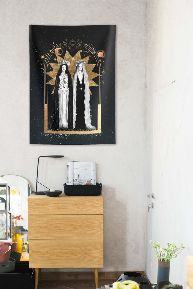 May include: A black tapestry with a gold frame and two figures in white dresses with long hair. The figures are standing in front of a large gold star with a crescent moon above it. The background is a dark blue with gold stars.