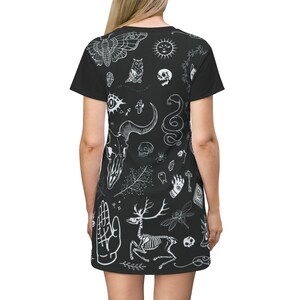 Może przedstawiać: Czarna sukienka t-shirt z białym nadrukiem r&oacute;żnych symboli okultystycznych i mistycznych, w tym czaszki, sowy, węża, szkieletu jelenia, ważki i dłoni z okiem.