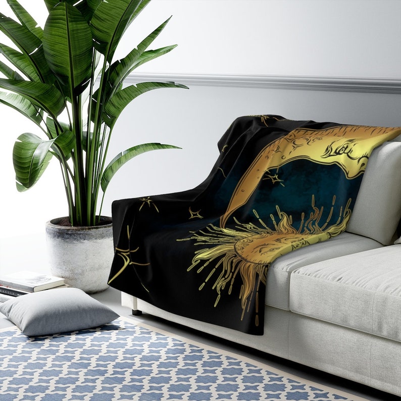 May include: A black throw blanket featuring a gold sun and moon design. The sun and moon are surrounded by stars and have a vintage, celestial feel.