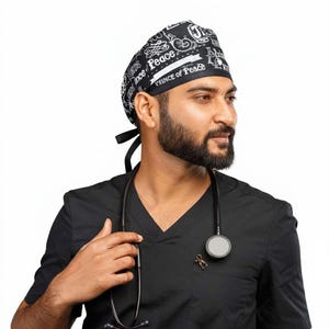 Op de afbeelding: Een zwart-wit patroon chirurgische scrub cap met de tekst "Prince of Peace" wordt gedragen met een zwarte scrub top. Een stethoscoop hangt om de nek.