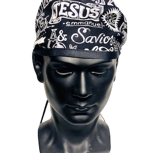 May include: Black and white patterned scrub cap with the words "GOD", "JESUS", "emmanuel", and "Savior" in a handwritten style. The cap has a black band around the bottom edge and is displayed on a black mannequin head.