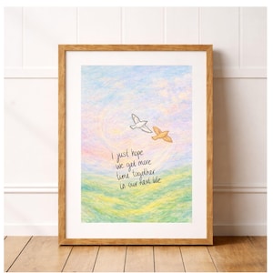 Op de afbeelding: Een ingelijste kunstdruk met een pastelkleurige lucht en een grasveld. Twee vogels worden in vlucht afgebeeld. De print bevat de handgeschreven tekst: "Ik hoop gewoon dat we meer tijd samen hebben in ons volgende leven."