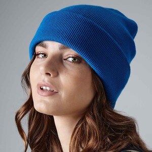 May include: A vibrant blue beanie hat. The hat is made of a ribbed knit fabric and is worn on the head. The beanie is a solid color and has a folded brim. The background is a solid gray.
