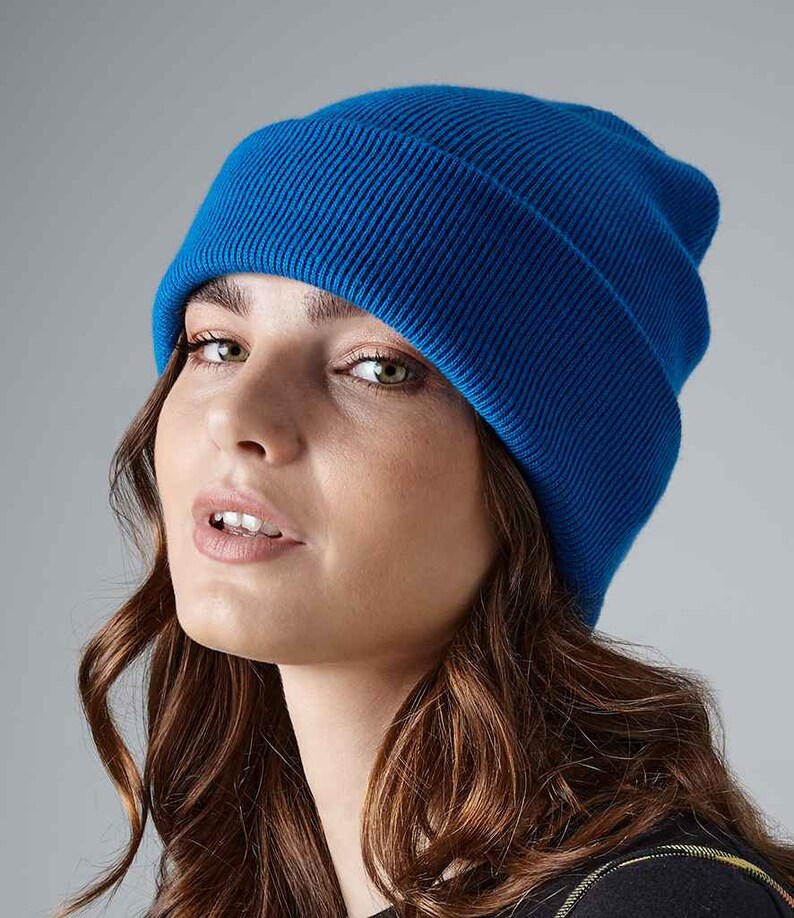 May include: A vibrant blue beanie hat. The hat is made of a ribbed knit fabric and is worn on the head. The beanie is a solid color and has a folded brim. The background is a solid gray.