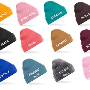 May include: A collection of twelve beanies in various colors, including orange, dusky pink, emerald, and chocolate. Each beanie has a folded cuff and a white text label indicating its color, such as "Orange" and "Black".
