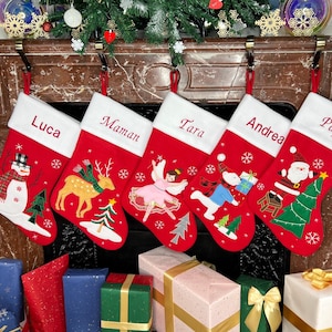 May include: Five red Christmas stockings with white cuffs hang above a fireplace. Each stocking has a name embroidered on it: Luca, Maman, Tara, Andrea, and Papa. The stockings feature festive designs like a snowman, deer, and Santa Claus.