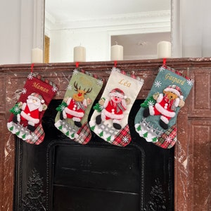 Può includere: Quattro calze natalizie decorative con personaggi festivi: Babbo Natale, renna, pupazzo di neve e orso. Ogni calza personalizzata porta un nome e presenta un motivo a quadri con fiocchi di neve e una piccola recinzione.