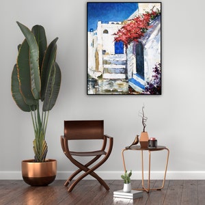 May include: A painting of a white building with a blue door and red flowers hanging over it. The building is in a narrow street with a blue sky in the background.