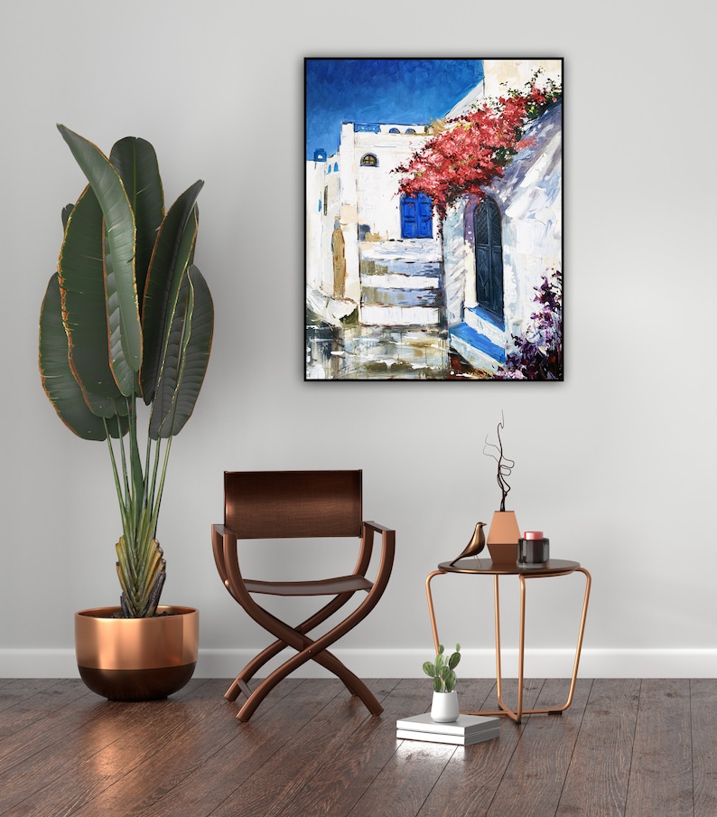 May include: A painting of a white building with a blue door and red flowers hanging over it. The building is in a narrow street with a blue sky in the background.