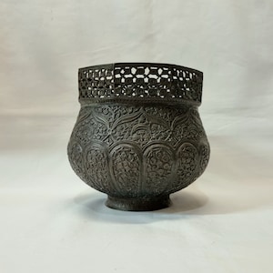 Può includere: Una ciotola in metallo grigio scuro con intricati disegni floreali e un bordo traforato decorativo.