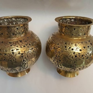 Op de afbeelding: Twee antieke messing vazen met ingewikkelde bloemmotieven en perforaties. De vazen zijn rond met een brede opening en een smalle basis.