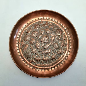 An antique Indian copper wall hanging plate profusely decorated with a theme of various types of birds in a sylvan and foliate setting.