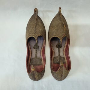 Pu&ograve; includere: Un paio di scarpe ornate in pelle marrone con intricati motivi in rilievo. Le scarpe hanno una punta affusolata e una tomaia curva, con interni rossi. Le scarpe sono probabilmente fatte a mano e hanno un design tradizionale.