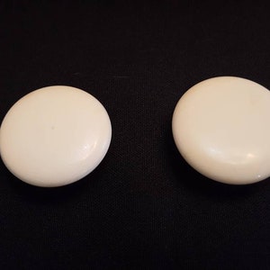 May include: Two white, round, smooth, ceramic knobs.