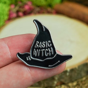 May include: Black enamel pin shaped like a witch's hat with the text "BASIC WITCH" on the front.