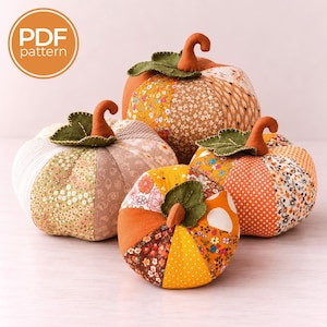Puede incluir: Tres calabazas de tela de varios tamaños, cada una construida con paneles de patchwork con patrones florales, de lunares y geométricos en naranja, amarillo, marrón y blanco. Cada calabaza tiene una hoja de fieltro verde y un tallo marrón.