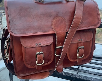 Könnte beinhalten: Eine braune Ledertasche mit zwei Fronttaschen und einem Schnallenverschluss. Die Tasche hat einen langen, verstellbaren Schultergurt und einen Tragegriff.