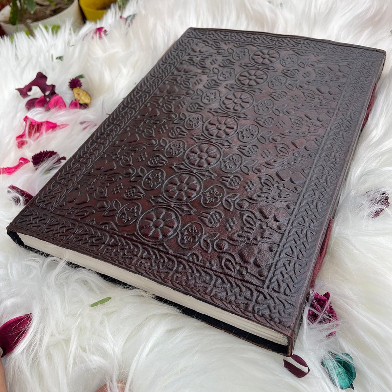 May include: A brown leather journal with an intricate embossed floral pattern. The journal has a blank page visible and is closed.