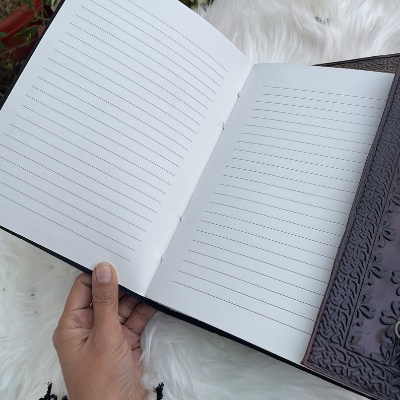 May include: A brown leather journal with a detailed embossed design on the cover. The journal is open to reveal lined pages.