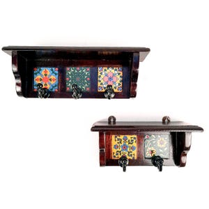 May include: Two dark wood key holders with decorative tiles. Each holder has a shelf and metal hooks. The tiles feature colorful floral patterns in blue, yellow, green, and pink. The hooks are black.