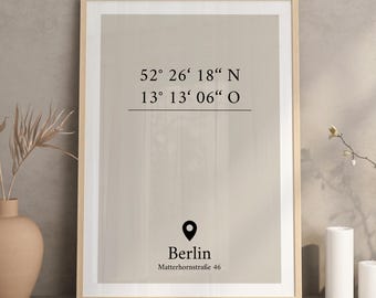 May include: A rectangular wall art print in a light wood frame featuring a beige background with black text. The print displays the coordinates 52° 26' 18" N 13° 13' 06" O, a location pin icon, the word Berlin, and the address Matterhornstraße 46.