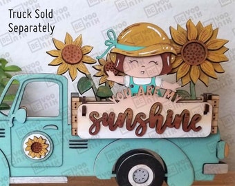 May include: A light blue toy truck with a wooden sign in the back that says "You are my sunshine". A girl with a yellow hat and a sunflower in her hand is sitting in the truck bed. The truck is on a wooden base.