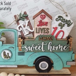 May include: A teal blue wooden truck with a white "hi" sign on the side. The truck bed is filled with wooden cutouts that say "Party of 10", "Love Lives", "Home Sweet Home", and a small house with a heart. The truck is sitting on a wooden base with a string of wooden beads.