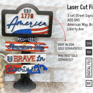 May include: Three wooden signs with red, white, and blue patriotic colors. The top sign says "Est 1776 America". The middle sign says "American Way". The bottom sign says "Brave Ln Liberty Ave".