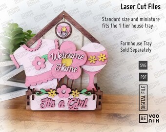 May include: Laser cut file for a wooden house shaped welcome home sign with a pink baby outfit, flowers, and a rattle. The sign says "Welcome Home" and "It's a Girl".