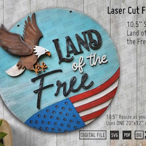 Könnte beinhalten: Ein rundes Holzschild mit einem amerikanischen Flaggen-Design in Blau und Rot. Das Schild trägt die Aufschrift "Land of the Free" in schwarzen Buchstaben mit einem Weißkopfseeadler, der obenauf sitzt. Das Schild ist zum Laserschneiden gedacht.
