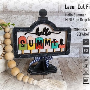 May include: A black wooden sign with a white background and the words "hello summer" in a white script font. The sign is decorated with colorful popsicle shapes and has a black stand. The sign is a laser cut file.