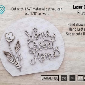 May include: A laser cut wooden sign with the text "Home Sweet Home" in a cursive font. The sign also features a small floral design with a single flower and leaves. The sign is on a white background and the text "Laser Cut Files" is in the top right corner.