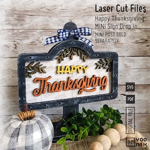 May include: A wooden sign with a black distressed finish and a white background. The sign says "Happy Thanksgiving" in orange and yellow letters. The sign is on a stand and has a bow with a blue and white checkered pattern.