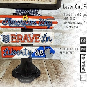 May include: Three wooden signs with red, white, and blue paint, featuring the text "American Way", "Brave Ln", and "Liberty Ave". The signs are attached to a black wooden post.