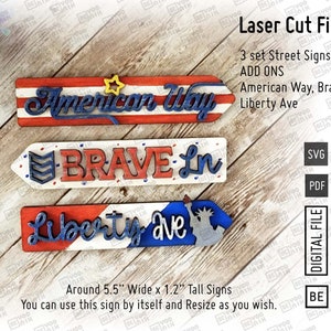 May include: Three laser cut wooden signs with red, white, and blue patriotic colors. The signs read "American Way", "Brave Ln", and "Liberty Ave". The signs are approximately 5.5 inches wide and 1.2 inches tall.