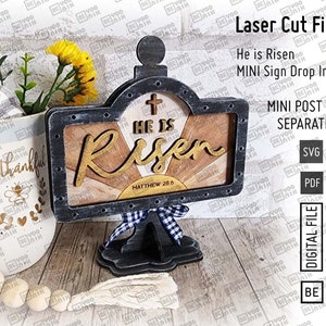 May include: Laser cut file design for a wooden sign that reads "He is Risen" with a cross and the scripture Matthew 28:6. The sign is in a rustic style with a black frame and a woodgrain background.