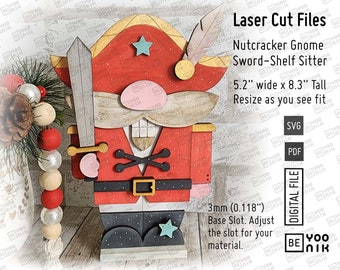 May include: Laser cut file design for a Nutcracker Gnome Sword-Shelf Sitter. The gnome is red, white, and black with a gold belt and a blue star on its foot. The gnome is holding a sword and has a beard and moustache. The design is 5.2 inches wide and 8.3 inches tall. The file is available in SVG and PDF formats. 3mm (0.118 inches) base slot. Adjust the slot for your material.
