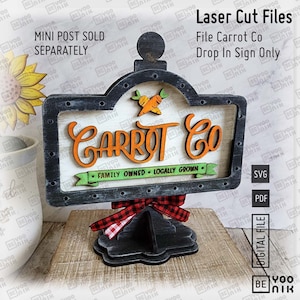 May include: A black and white wooden sign with the text "Carrot Co." in orange lettering. The sign has a green banner with the text "Family Owned - Locally Grown". The sign is attached to a black wooden stand with a red and black checkered bow.