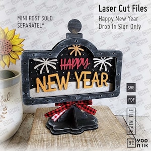 May include: Black and white laser cut wood sign with the text "Happy New Year" in red and gold letters. The sign is decorated with fireworks and has a black and red checkered bow. The sign is on a black stand.