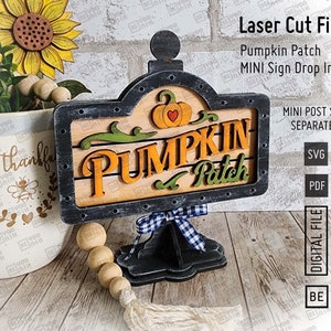 Puede incluir: Archivos de corte láser para un letrero de parche de calabaza. El letrero es negro con un diseño de parche de calabaza de madera y las palabras "Pumpkin Patch" en letras naranja y marrón. El letrero está en un soporte negro con un lazo azul y blanco a cuadros.