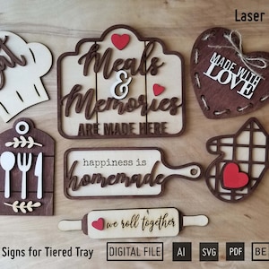 May include: Seven wooden signs with various kitchen-themed sayings, including "Meals & Memories Are Made Here", "Happiness is Homemade", and "We Roll Together". The signs are designed for a tiered tray and are available as digital files in AI, SVG, and PDF formats.