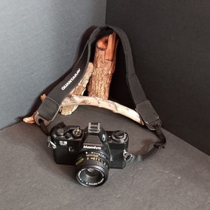 May include: A black Mamiya camera with a black strap that says "QUANTARAY" on it. The camera is sitting on a wooden surface.