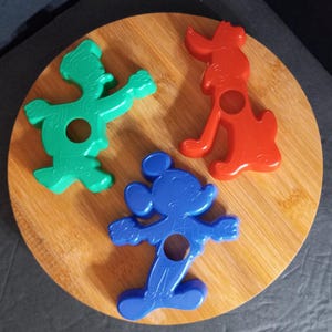 May include: Three plastic cookie cutters shaped like Mickey Mouse, Donald Duck, and Pluto. The cutters are blue, green, and red.