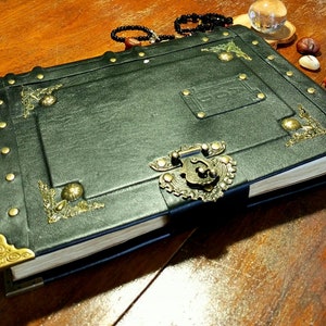 Puede incluir: Un diario de cuero verde oscuro con adornos de lat&oacute;n ornamentados, incluyendo una cerradura y una cerradura. El diario tiene un aspecto desgastado y vintage y est&aacute; cerrado.