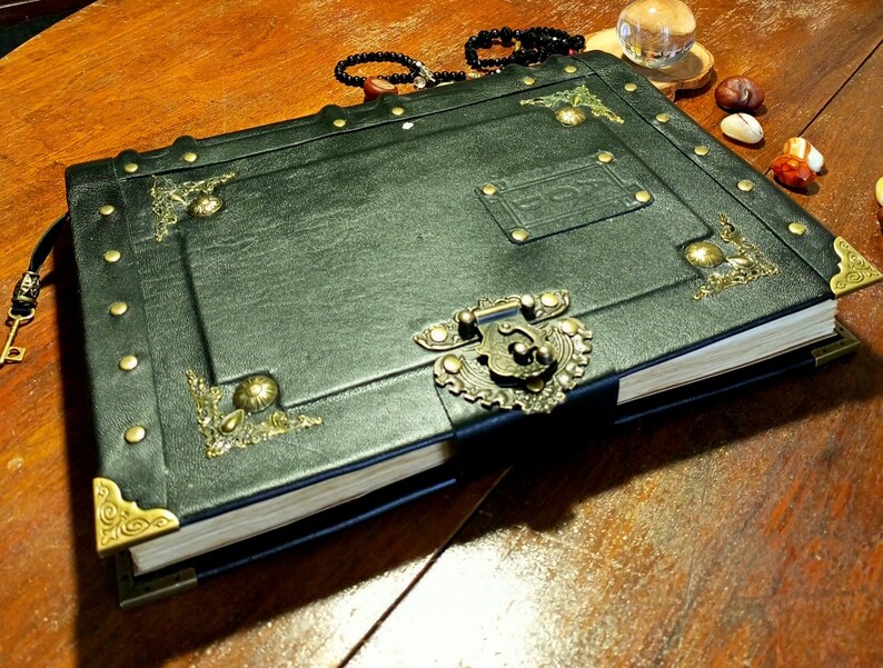 Puede incluir: Un diario de cuero verde oscuro con adornos de lat&oacute;n ornamentados, incluyendo una cerradura y una cerradura. El diario tiene un aspecto desgastado y vintage y est&aacute; cerrado.