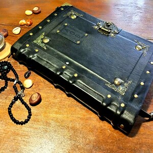 Puede incluir: Un diario encuadernado en cuero negro con detalles dorados y una cerradura y llave de lat&oacute;n. El diario tiene una etiqueta en la parte delantera que dice "HOD".