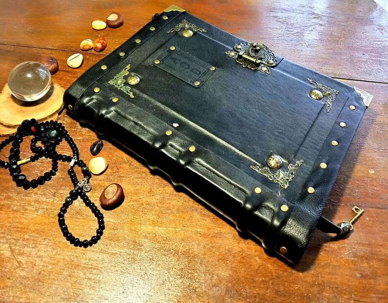 Puede incluir: Un diario encuadernado en cuero negro con detalles dorados y una cerradura y llave de lat&oacute;n. El diario tiene una etiqueta en la parte delantera que dice "HOD".