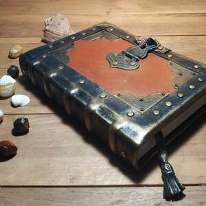 May include: A brown leather-bound journal with a metal clasp and decorative accents. The journal has a distressed look and a tassel.