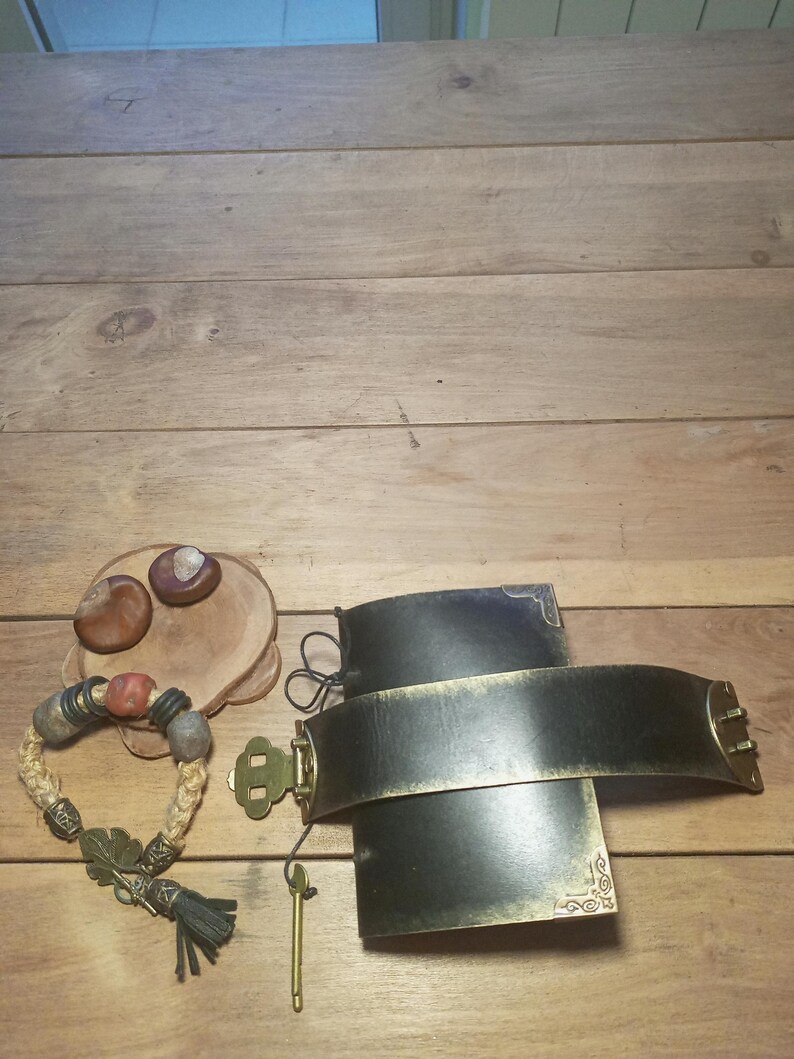 May include: A collection of handcrafted items on a wooden surface. Includes a black leather cuff with brass accents, a beaded bracelet with natural stone beads, and a small wooden coaster with chestnuts.