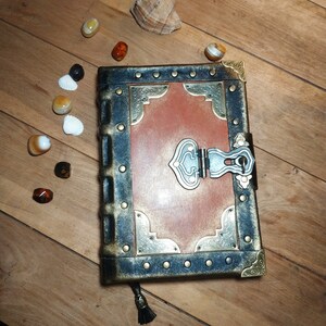 May include: A brown leather-bound journal with a decorative metal clasp and ornate metal accents. The journal has a distressed look and is closed.
